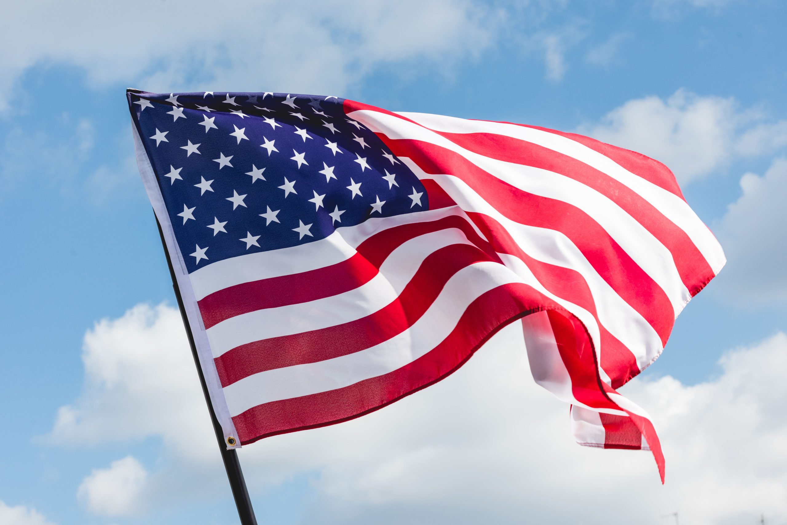 American flag flying with a blue sky and clouds in the background