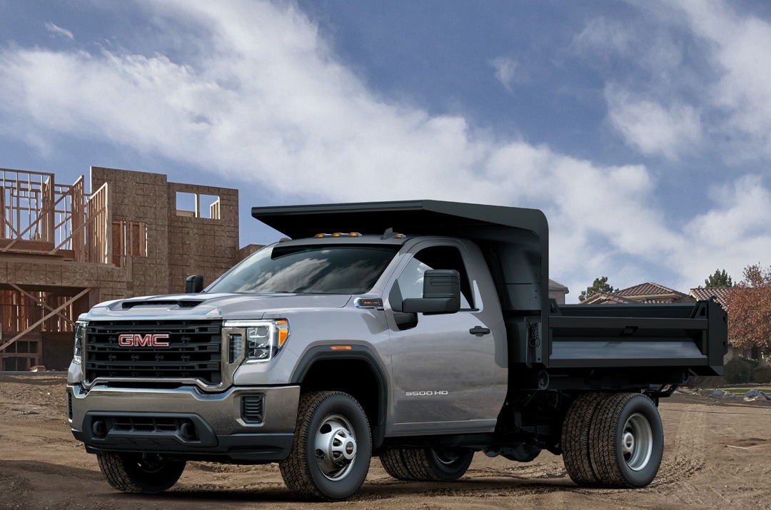 2024 GMC 3500 HD chassis cab truck with a dump truck rear parked in front of a construction site